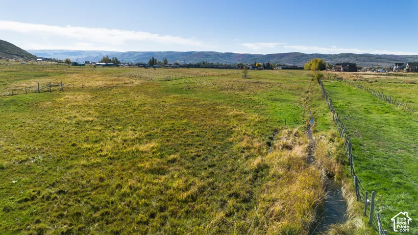 Expansive green fields with distant mountainous terrain, perimeter fencing, and a visible water channel