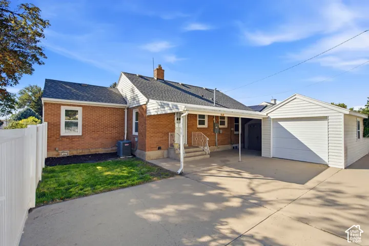 Brick exterior with a detached garage, covered carport, concrete driveway, and white picket fence. One car garage