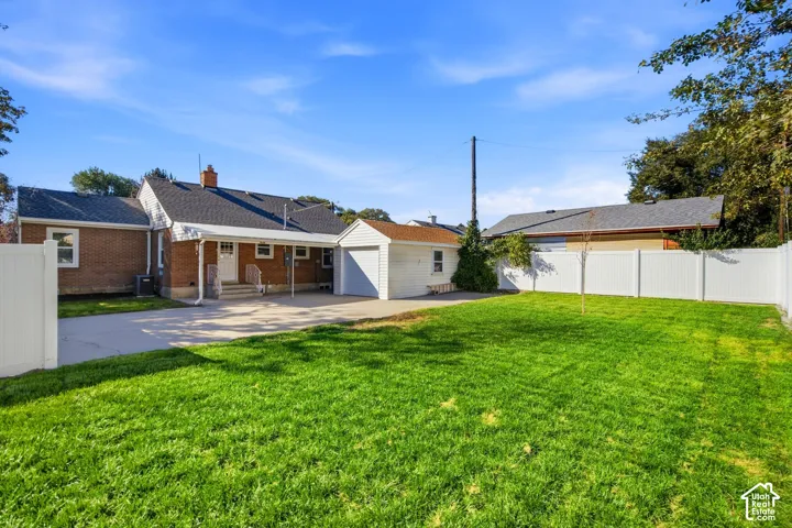 Expansive green lawn, white privacy fencing, paved driveway, covered patio, and detached one car garage