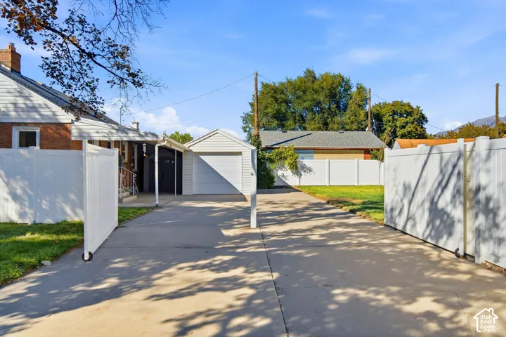 Concrete driveway with a detached garage, carport, white privacy fencing, large gate for RV entrance and parking.