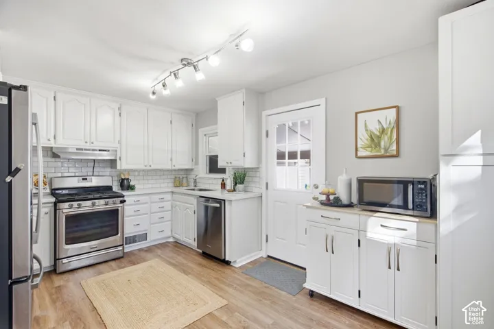 White cabinetry with stainless steel appliances, light wood-finish flooring, and subway tile backsplash