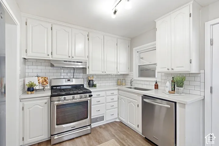 White cabinetry with brushed nickel hardware, stainless steel gas range, subway tile backsplash, stainless steel dishwasher, and wood-finish flooring