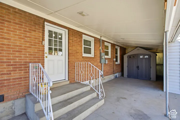 Covered concrete patio with a brick exterior, white paneled door, and a storage shed