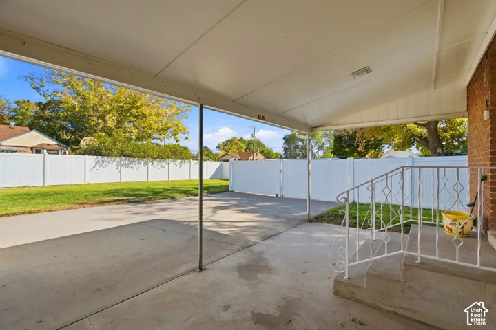 Covered patio area with a concrete surface, white vinyl fencing, and a manicured lawn