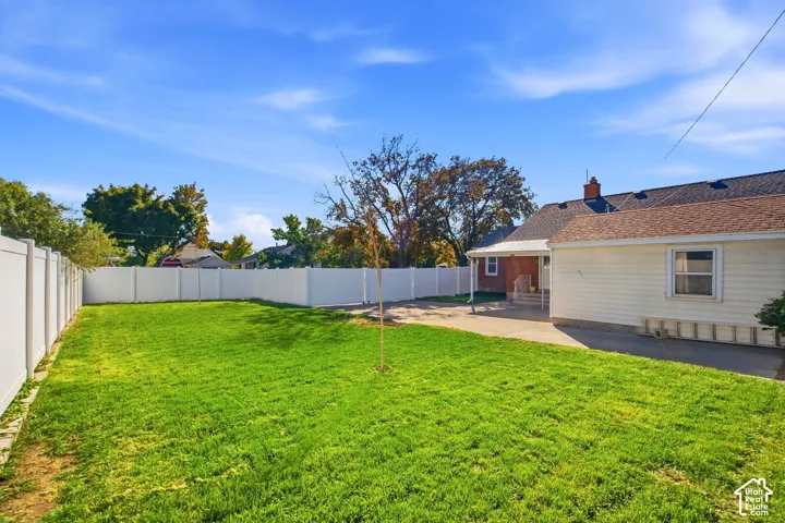 Expansive lawn area with a new white vinyl fence, a concrete patio, and a covered back porch