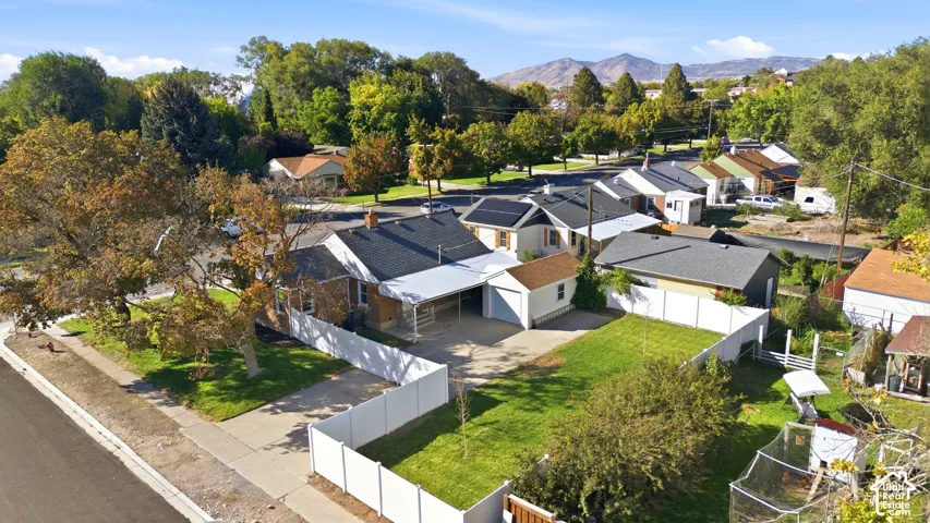 Paved driveway with an attached carport, front yard with mature trees, and white privacy fencing