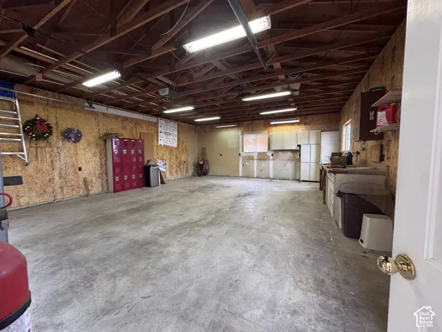 Concrete flooring in a spacious utility area featuring exposed wood rafters and fluorescent lighting
