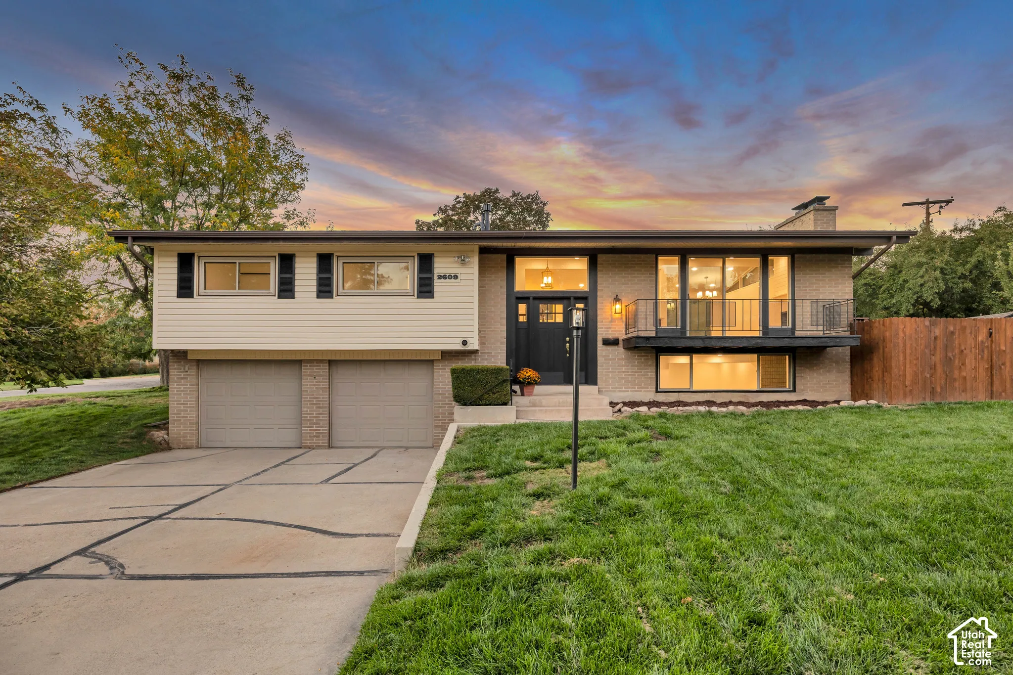 Split-level residence featuring a two-car garage, brick and siding exterior, front balcony with metal railing, and an expansive concrete driveway