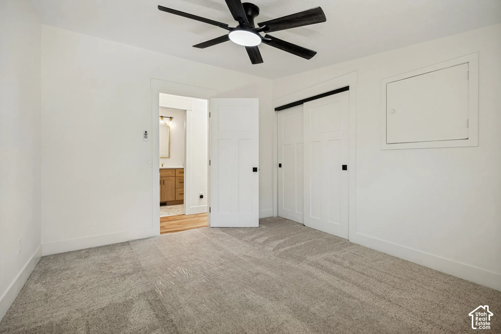Carpeted flooring, contemporary ceiling fan, white paneled barn doors, and natural wood vanity in the background