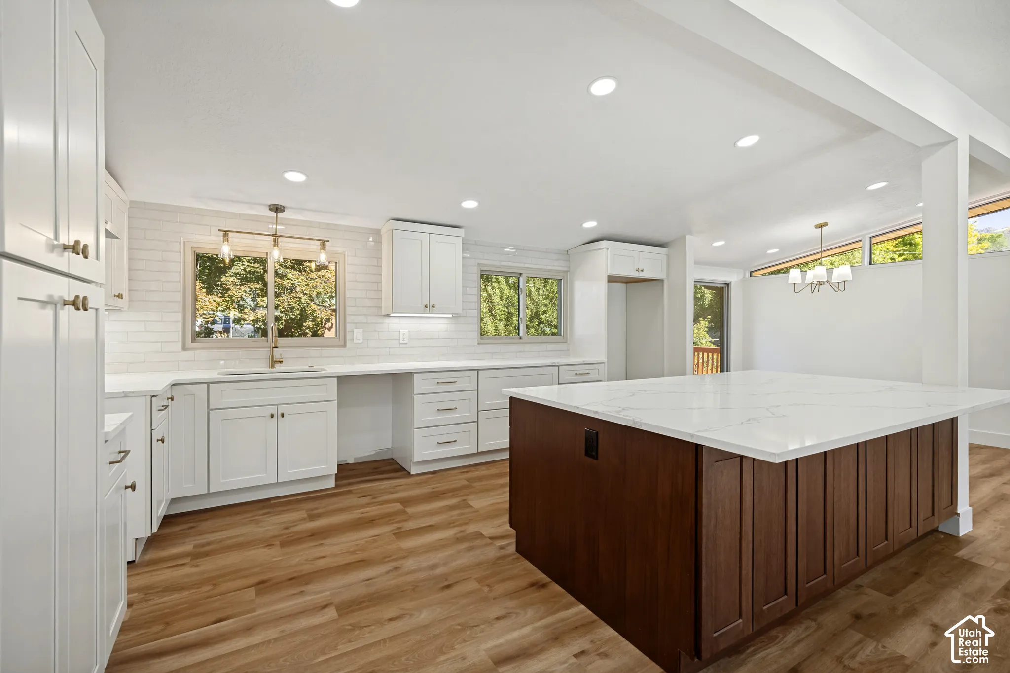Spacious kitchen featuring white cabinetry, a large center island with a stone-finish countertop, wood-finish flooring, and subway tile backsplash