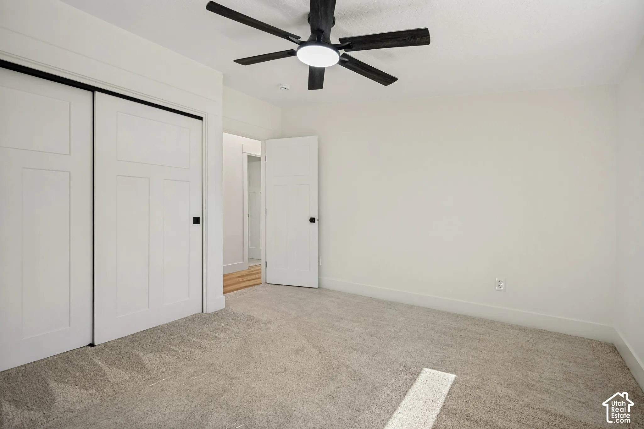 Wall-to-wall carpeting with light-toned walls, white panel doors, and a ceiling fan with integrated lighting