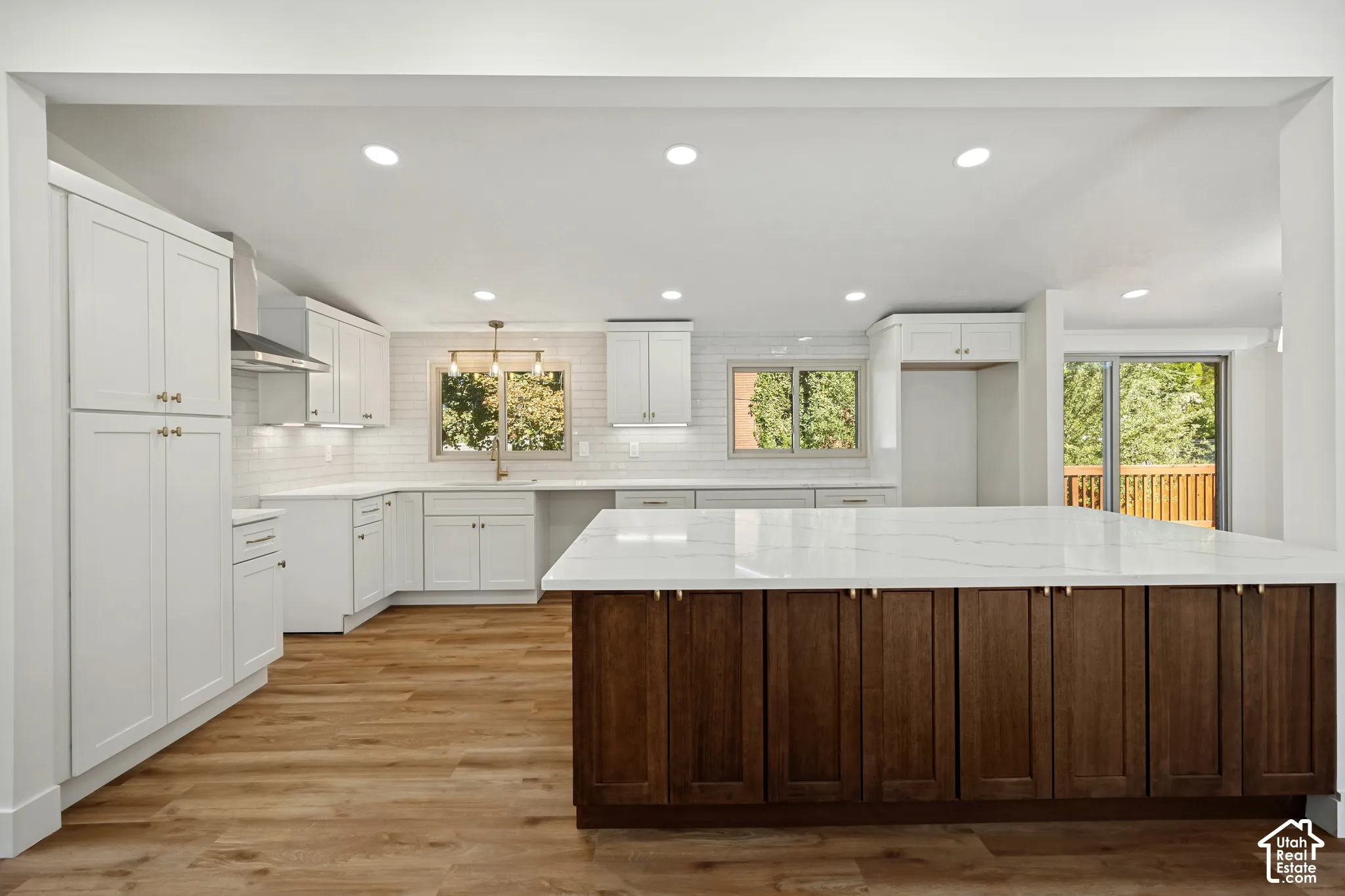 Contemporary kitchen featuring white shaker cabinetry, an expansive central island with dark wood-finish cabinetry and light-toned countertop, wood-finish flooring, and recessed lighting