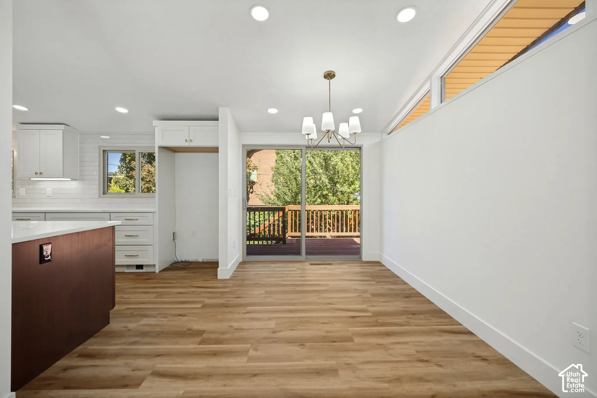 Wood-finish flooring throughout, white shaker cabinetry, white subway tile backsplash, white countertops, and a sliding glass door leading to a wood deck