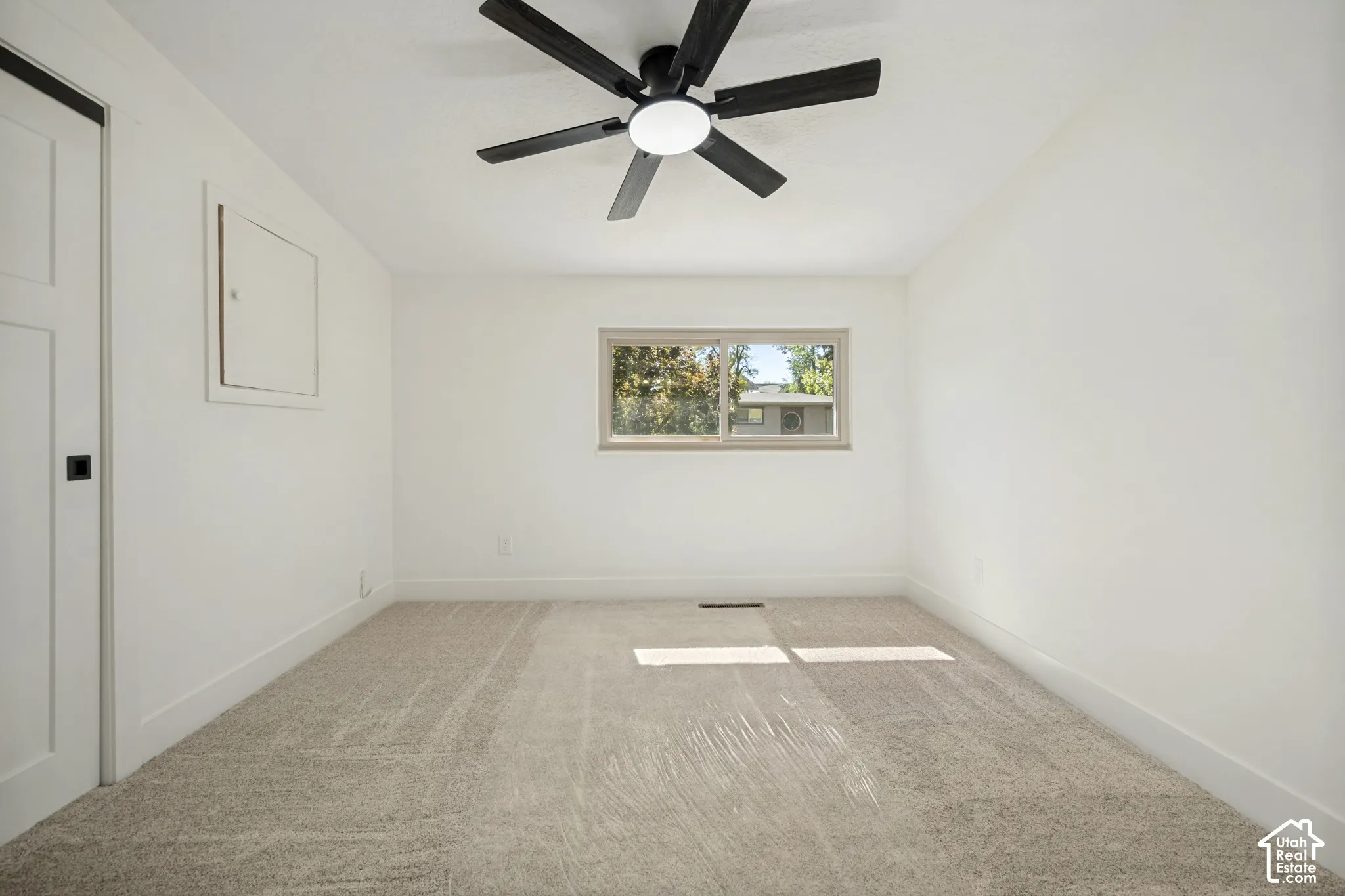 Plush carpeting, a modern ceiling fan with lighting, and a window with exterior scenery
