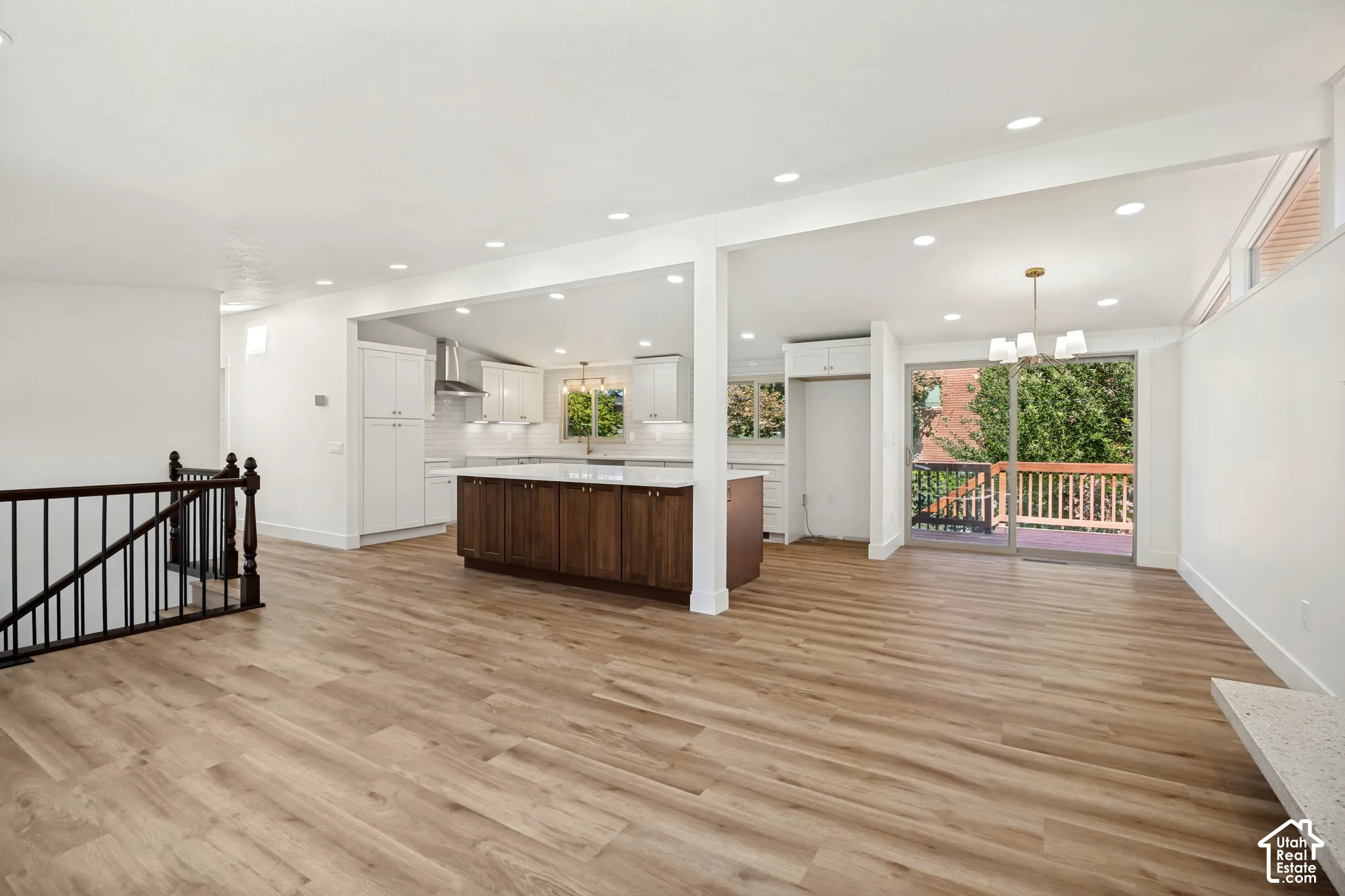 Wood-finish flooring throughout, white walls, recessed ceiling lights, white shaker-style cabinetry with stainless steel appliances, and a wood-finish island with a light-colored countertop