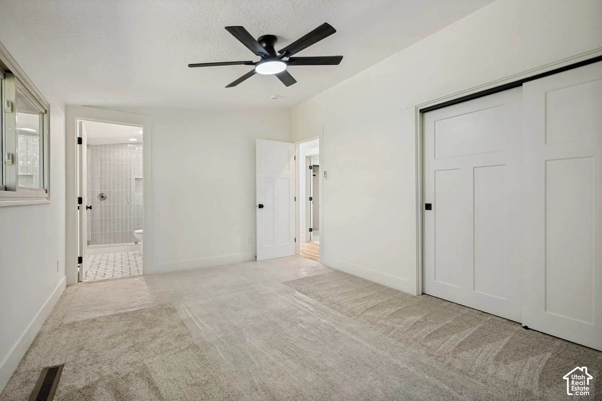 Carpet flooring, ceiling fan, white paneled doors, sliding closet doors, and an en-suite bathroom with tiled flooring