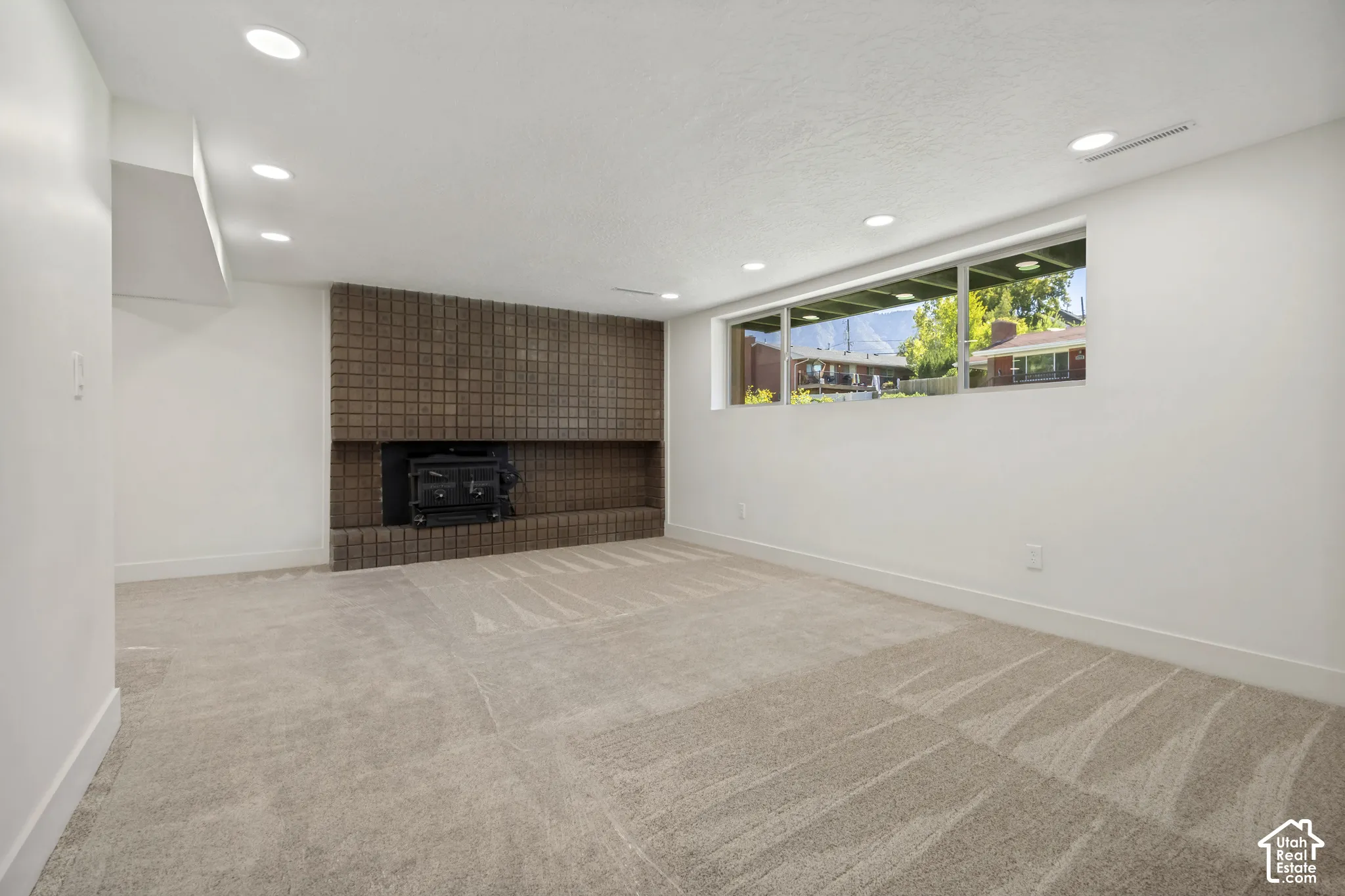 Expansive room featuring recessed lighting, a brick fireplace with a wood-burning stove, and a wall of windows