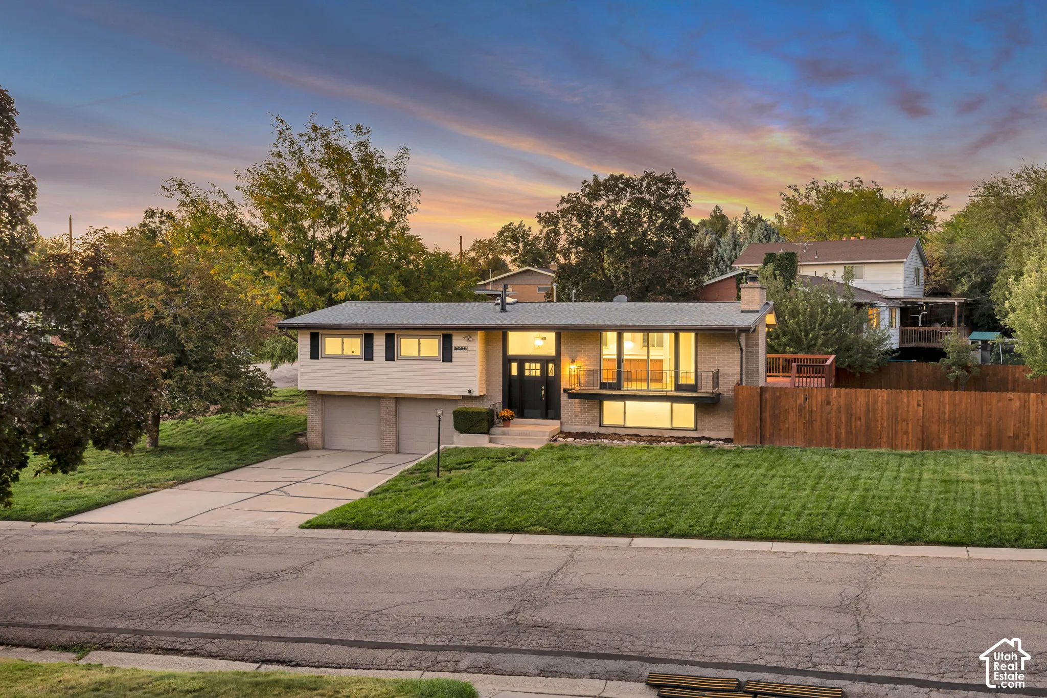 Split-level residence featuring brick and siding exterior, two-car garage, expansive front lawn, and a privacy fence