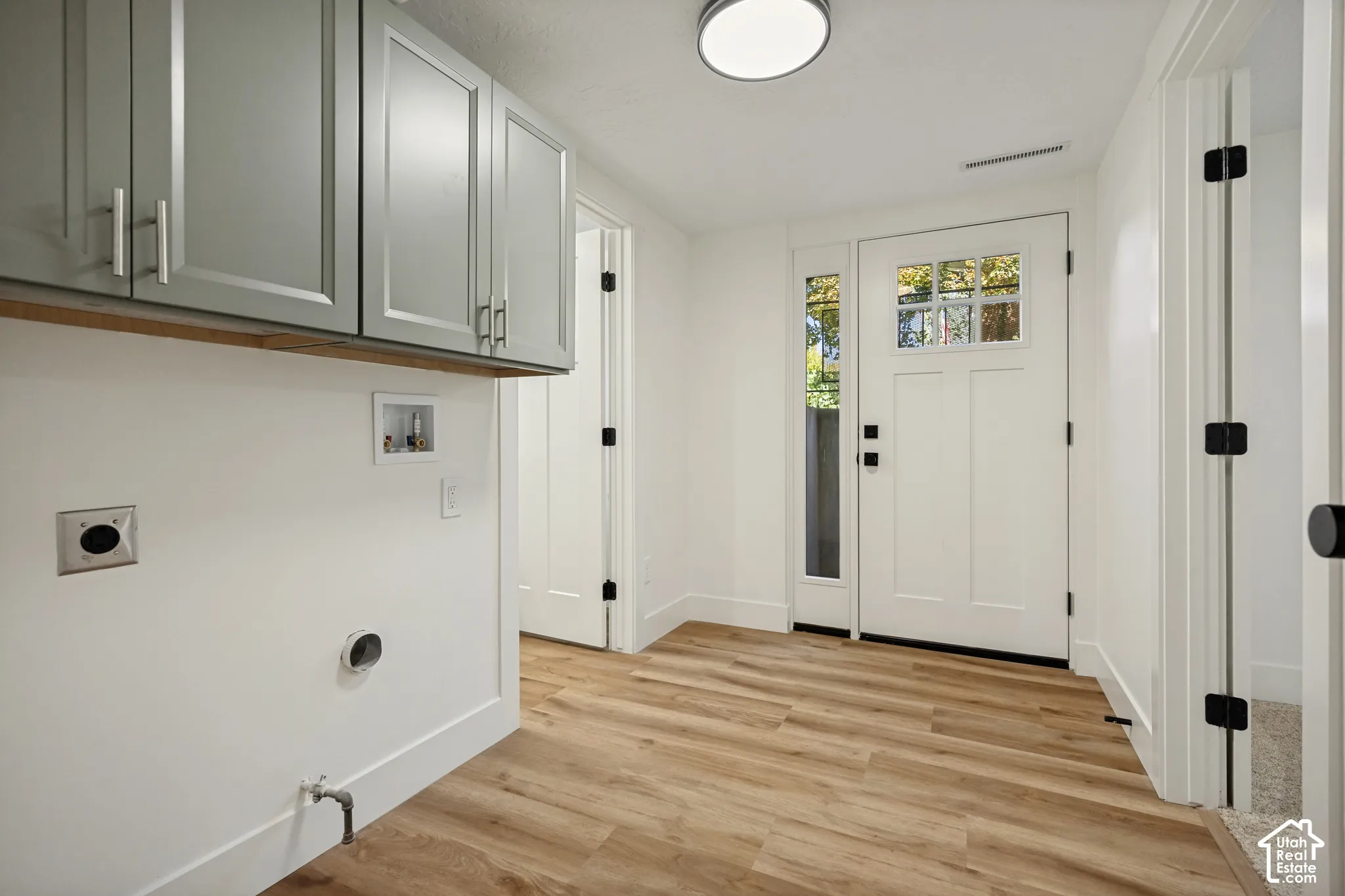 Wood-finish flooring throughout, white baseboards, and a white entry door with clear glass panels