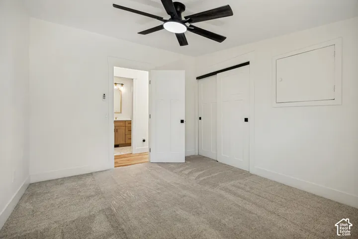 Carpeted flooring, contemporary ceiling fan, white paneled barn doors, and natural wood vanity in the background