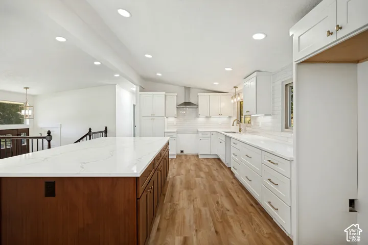 Spacious kitchen featuring an expansive island with a stone-finish countertop, wood-finish flooring, white shaker cabinetry, and recessed lighting