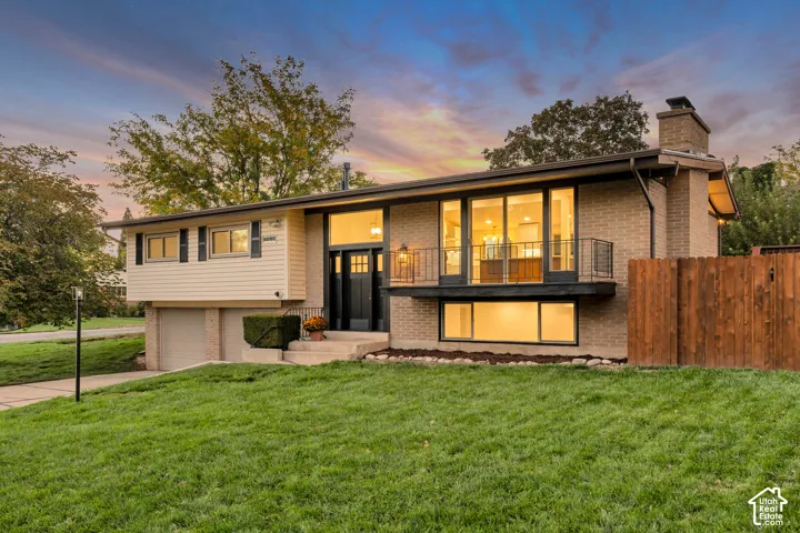 Brick and siding exterior with a prominent chimney, a front balcony with black railing, and a multi-pane entry door