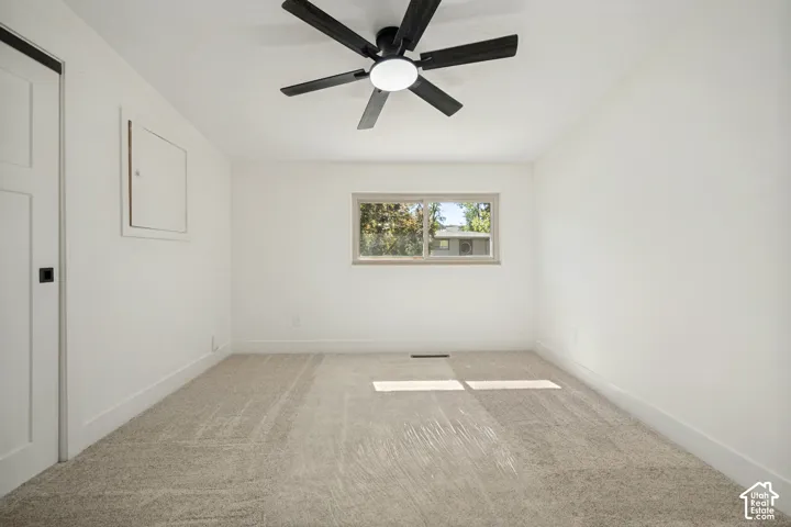 Plush carpeting, a modern ceiling fan with lighting, and a window with exterior scenery