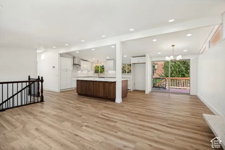 Wood-finish flooring throughout, white walls, recessed ceiling lights, white shaker-style cabinetry with stainless steel appliances, and a wood-finish island with a light-colored countertop