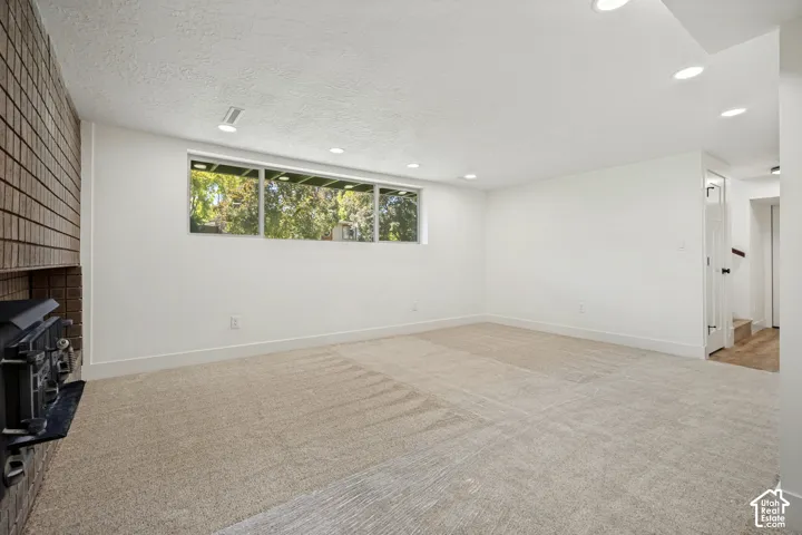 Recessed lighting, wood-burning stove with brick surround, wall-to-wall carpeting, and wood-finish flooring in hallway