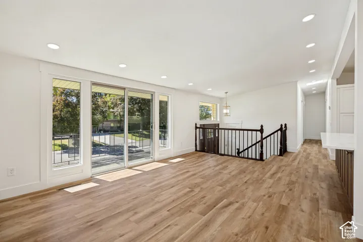 Expansive living area featuring wood-finish flooring, recessed lighting, white walls, a staircase with dark wood newel posts and railings, and a sliding glass door leading to a balcony