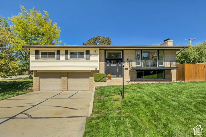 Split-level residence featuring a two-car garage, brick and siding exterior, front balcony with metal railing, and a concrete driveway