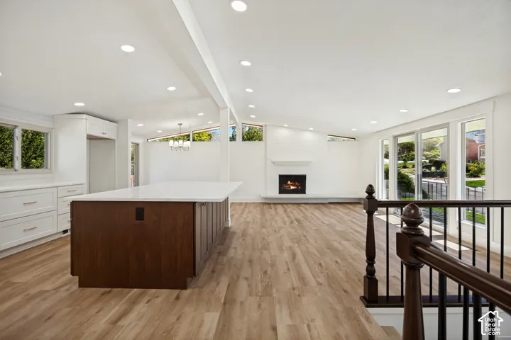 Open-concept living area featuring wood-finish flooring, a white-painted fireplace, extensive windows, recessed lighting, and a kitchen island with a light-toned countertop