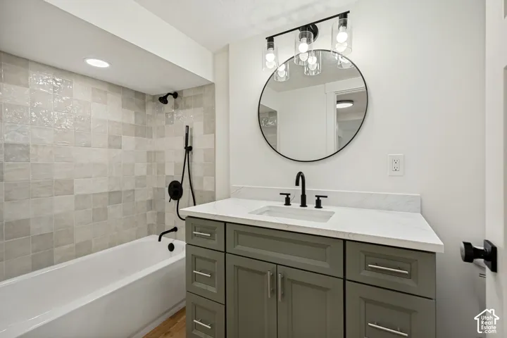 Bathtub with tiled surround, matte black shower fixtures, and recessed lighting