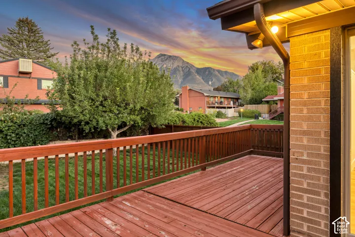 Expansive wood deck with wood railing, featuring a brick exterior and a background mountain range