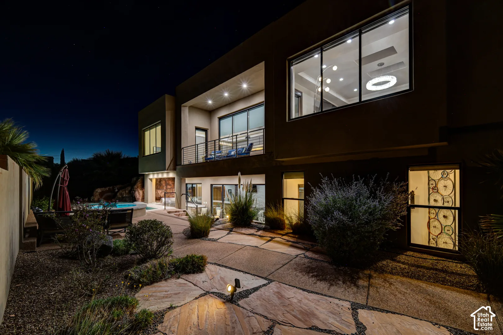 Multi-story exterior with a second-level balcony, ground-level patio with flagstone pavers, and an integrated pool area