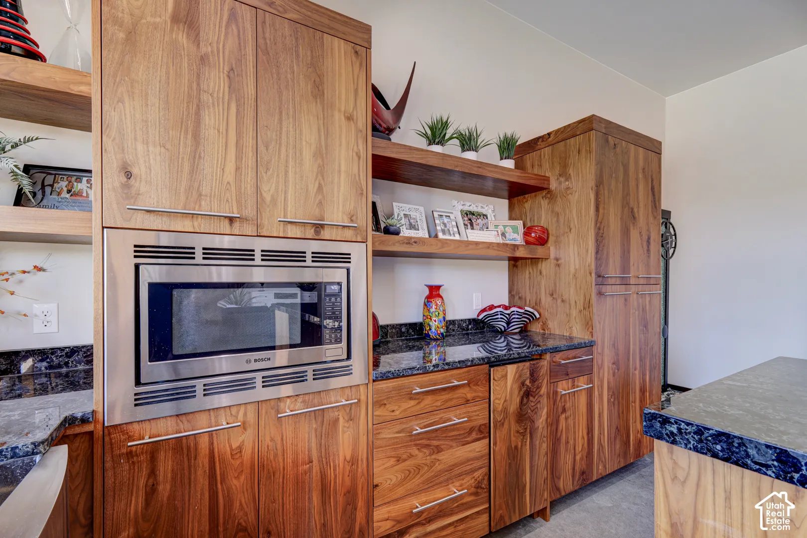 Built-in stainless steel microwave, wood-finish cabinetry, dark stone countertops, and open shelving