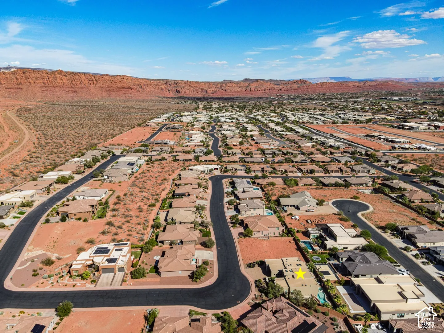 Aerial perspective showcasing residential properties and undeveloped lots with desert landscaping, surrounded by expansive red rock formations