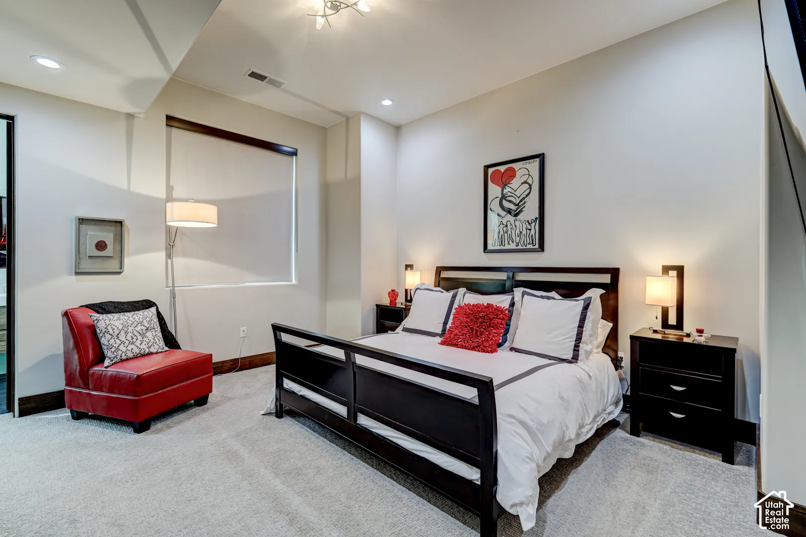 Recessed lighting, light-colored walls, carpeted flooring, and a large window with roller shades
