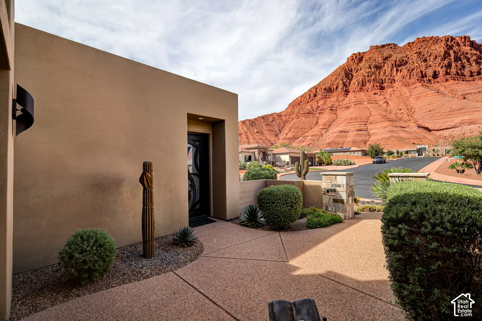 Stucco exterior with a modern sconce light, decorative desert landscaping, and a red rock mountain backdrop