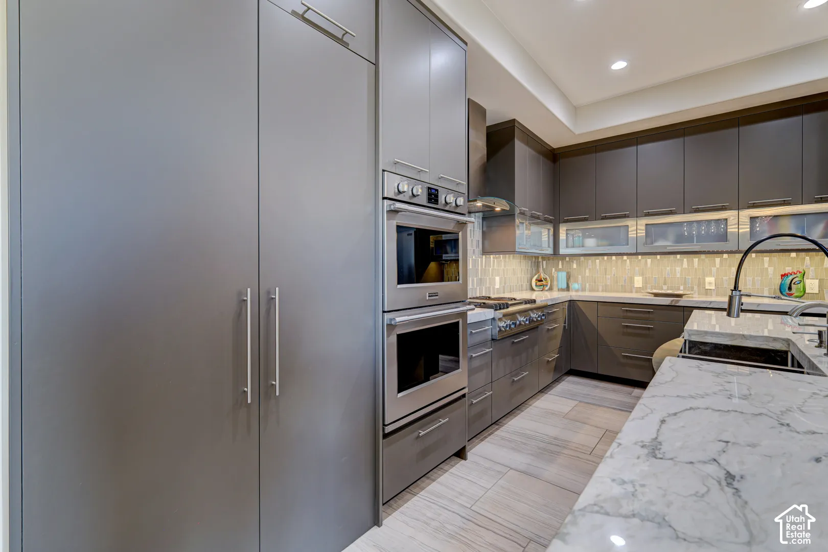Modern kitchen featuring integrated panel appliances, double wall ovens, a gas range with a vent hood, and stone countertops