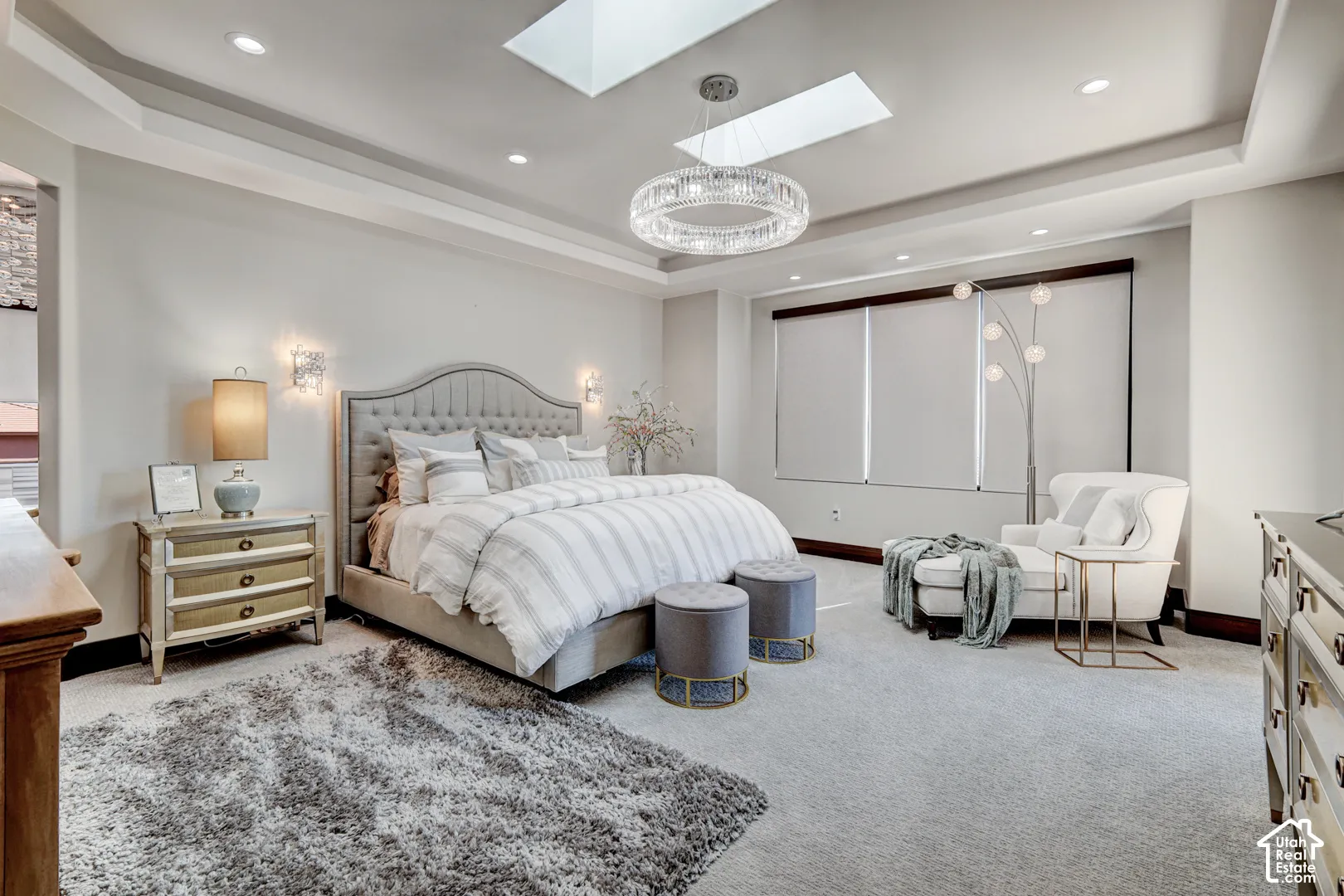 Tray ceiling with recessed lighting, skylight, chandelier, and a tufted headboard