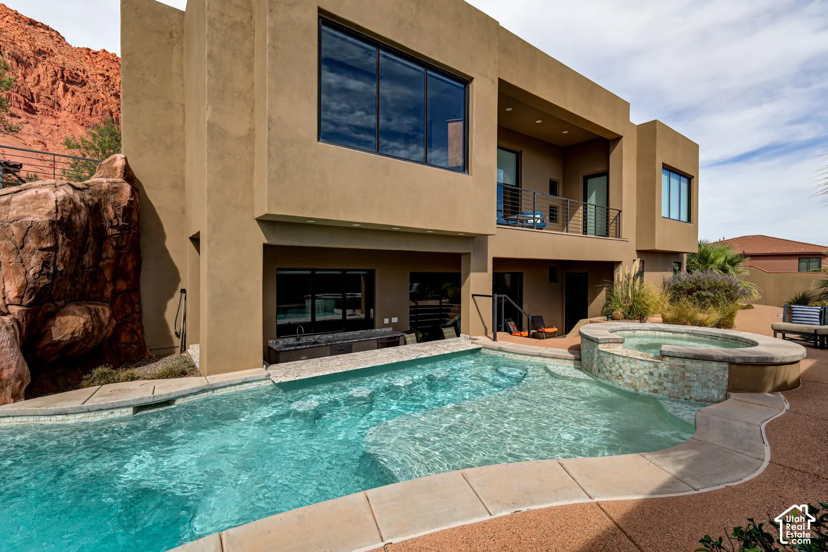 Contemporary stucco exterior featuring a tiered design, a rectangular pool, a tiled spa, a second-story balcony with metal railings, and a built-in outdoor counter