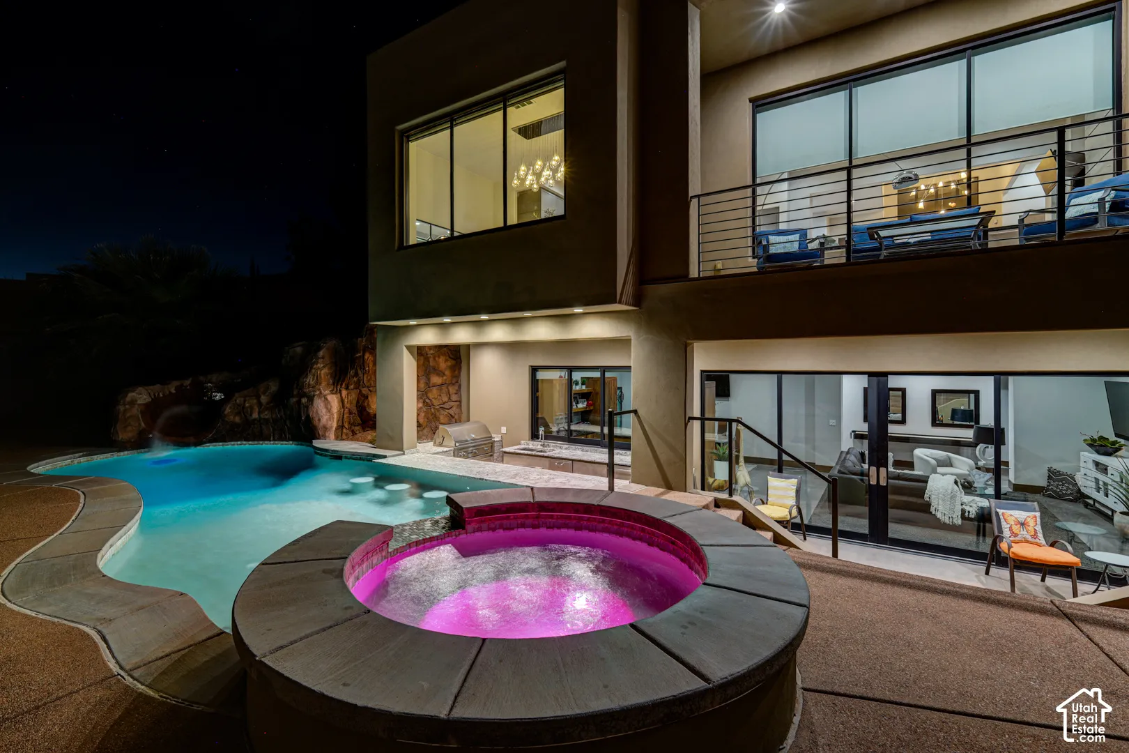 Multi-level modern exterior featuring a built-in spa, freeform swimming pool with rock waterfall, built-in outdoor kitchen, and a second-story balcony with metal railings