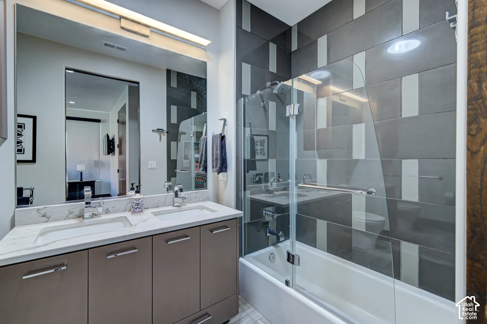 Dual vanity with stone-finish countertop and undermount sinks, glass shower enclosure, and tiled shower surround with accent pattern