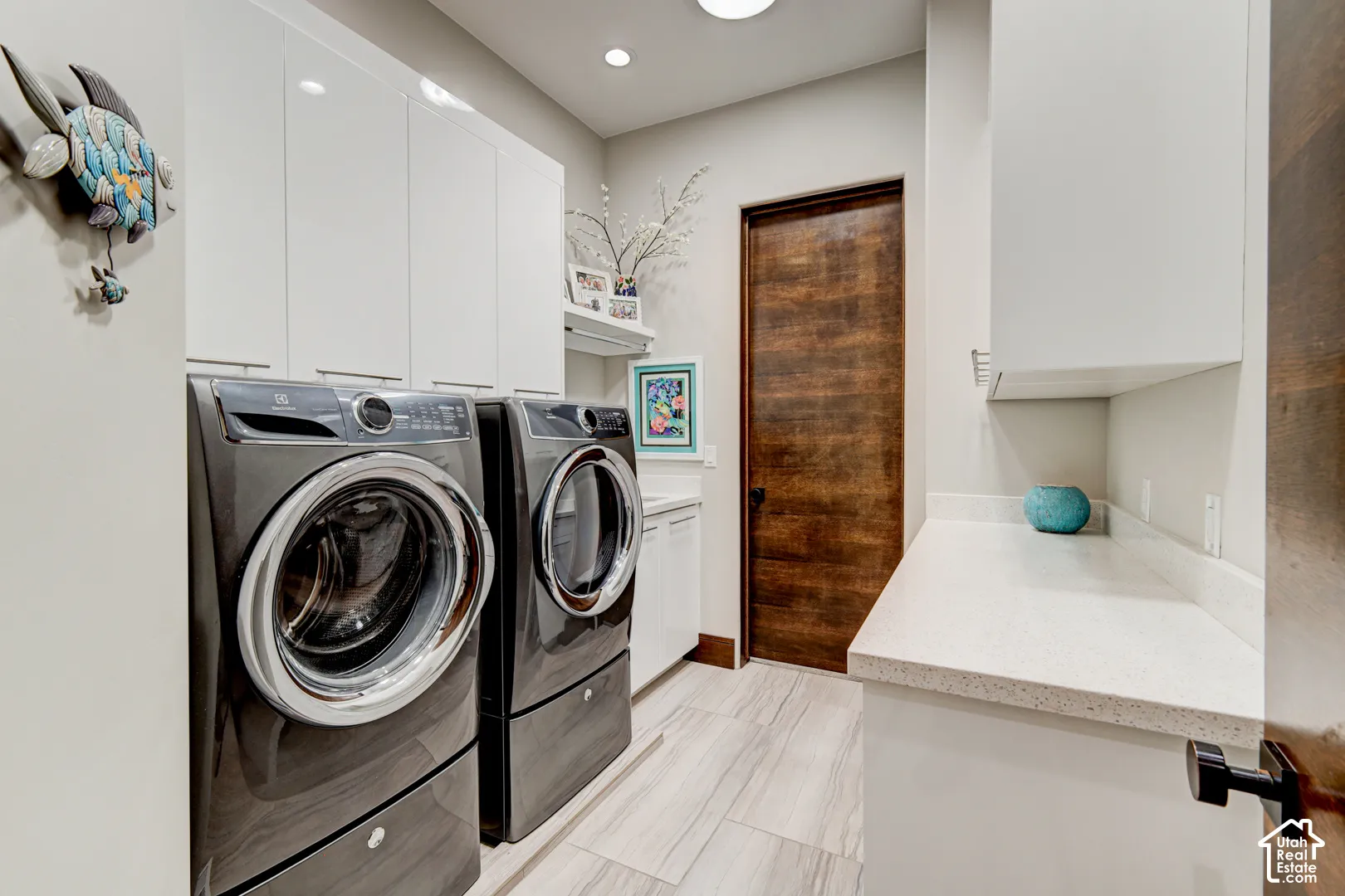 Laundry area featuring light wood-finish flooring, white cabinetry, a built-in countertop, and a wood-finish door