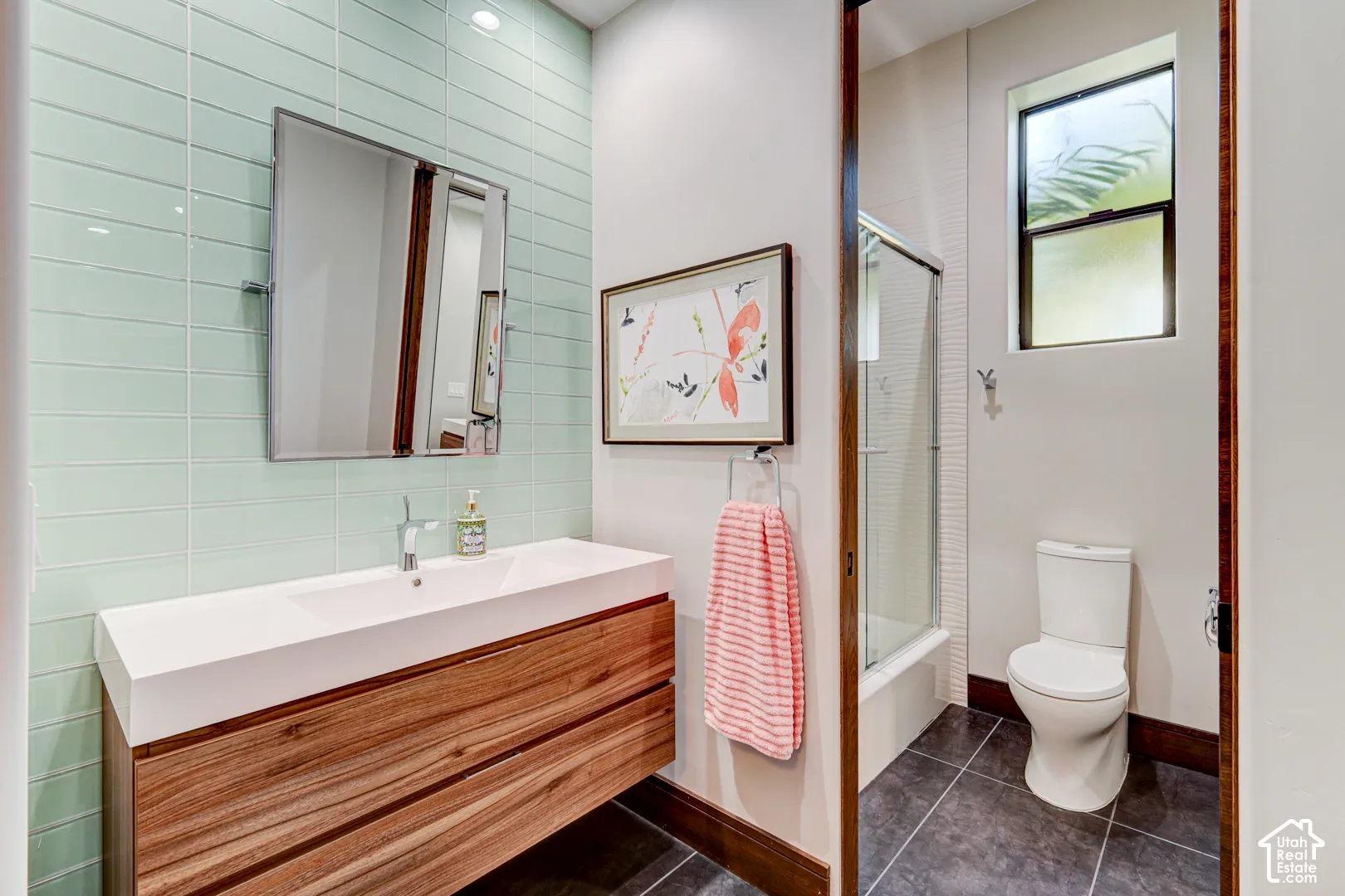 Floating wood-finish vanity with an integrated basin sink, light green subway tile backsplash, and a glass-enclosed shower