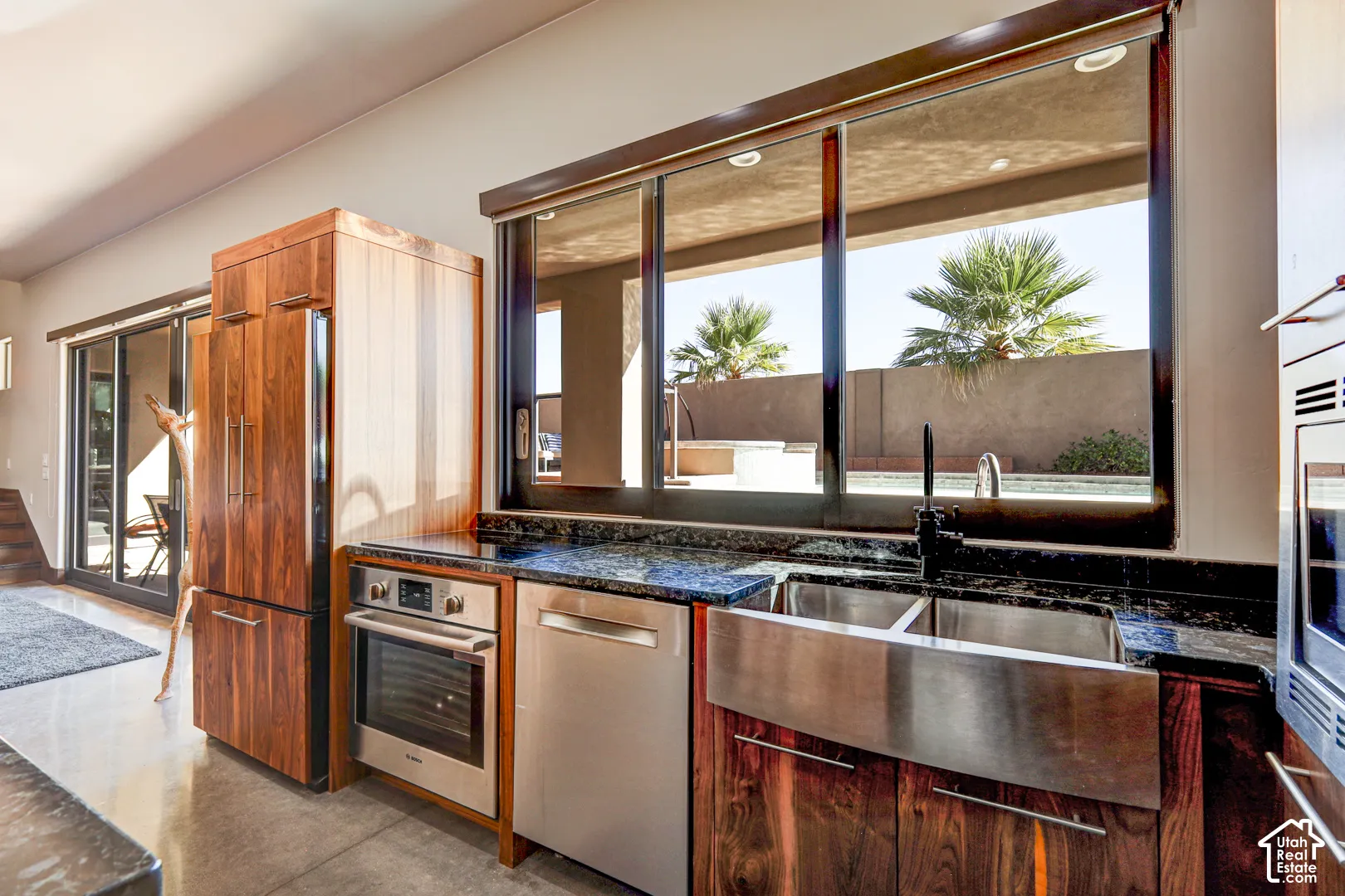 Kitchen featuring wood-finish cabinetry, stainless steel appliances, a dark stone countertop, and a stainless steel farmhouse sink