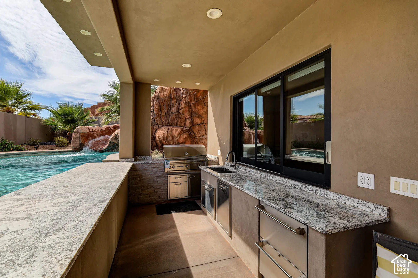 Covered outdoor kitchen featuring granite countertops, stainless steel appliances, a built-in grill, and a sliding window