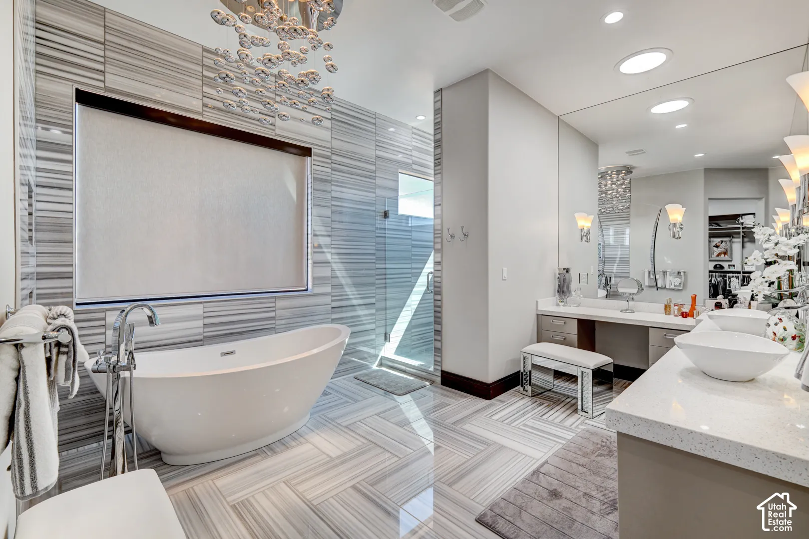 Freestanding bathtub with floor-mounted faucet, glass-enclosed shower, dual vanity with vessel sinks, and integrated lighting