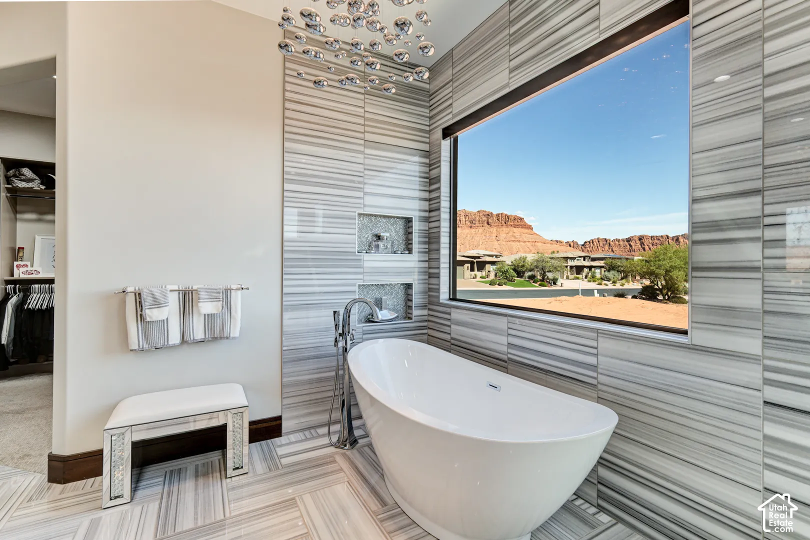 Freestanding soaking tub with floor-mounted faucet, striped tile surround, and large picture window